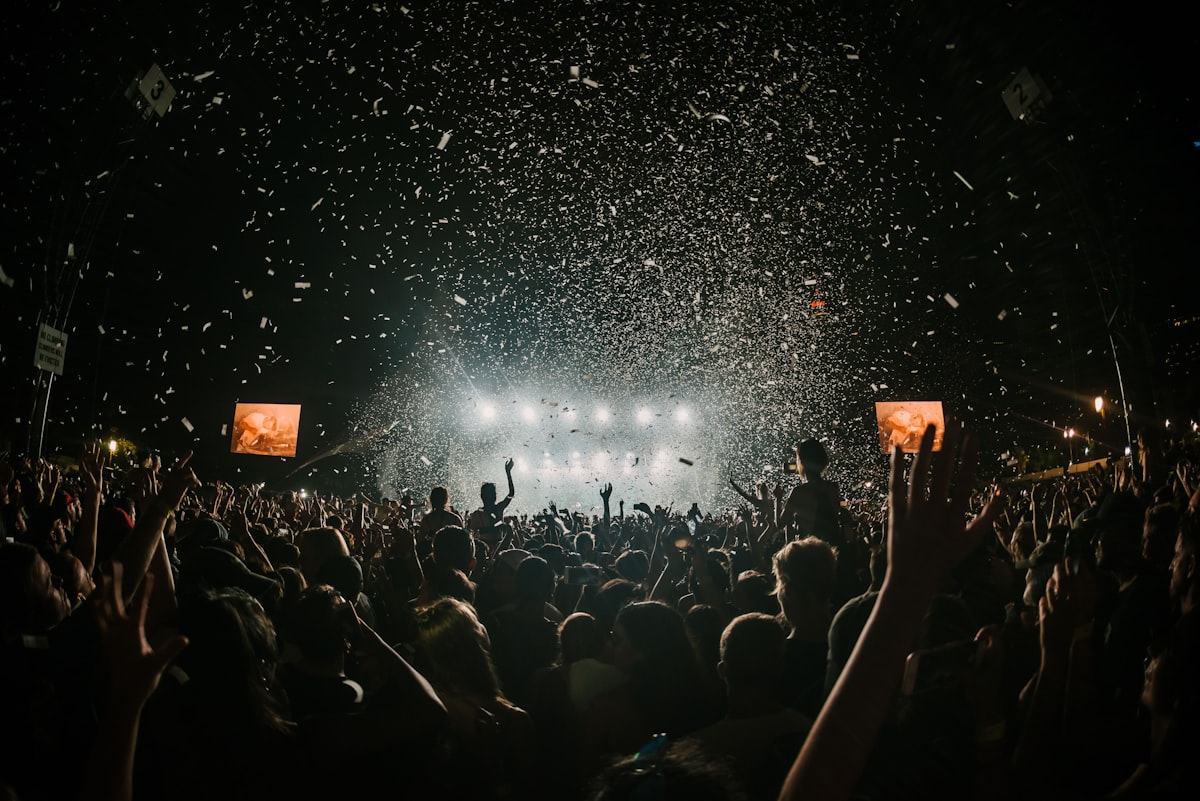 Festival crowd with hands raised under confetti and stage lights