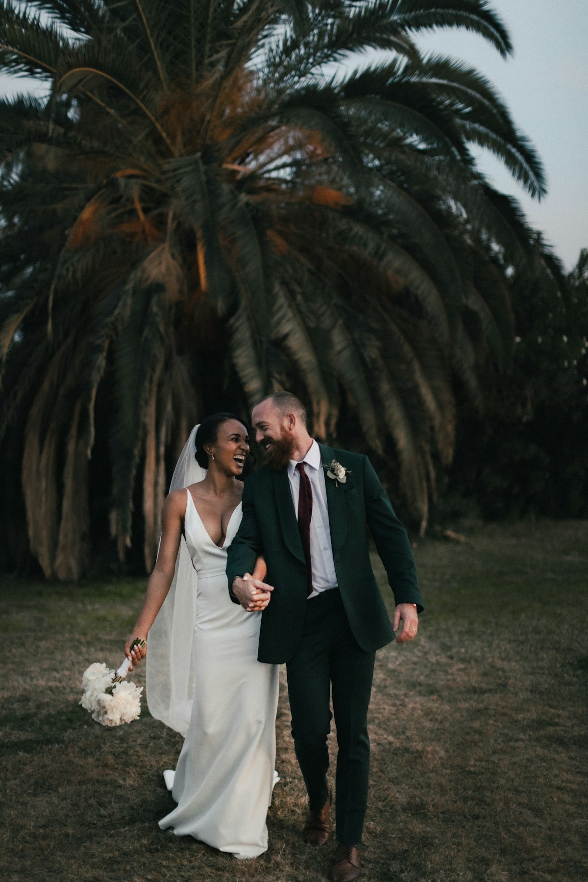 Wedding couple laughing together beneath a palm tree